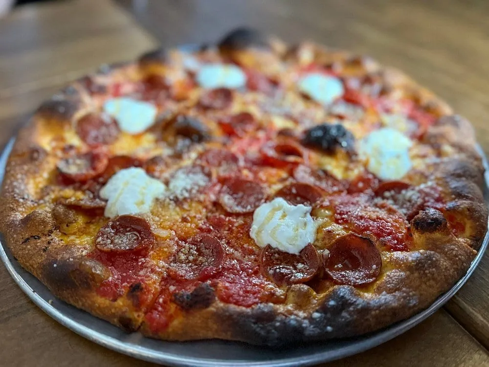 A New Haven-style pepperoni pizza at Crisp in Mayfair, its crust blistered and charred dark at the edge, topped with cupped pepperoni, tomato and spoonfuls of ricotta, on a metal pan